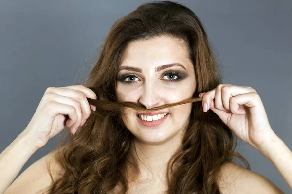 Attractive face of young girl with  make-up  holds hair as moustaches and smile — Stock Photo, Image