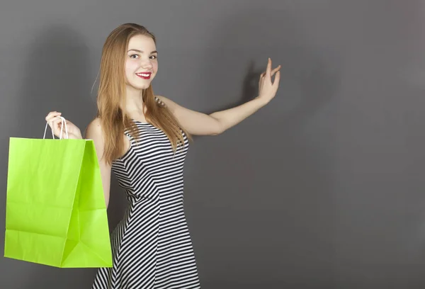 Mosolygós kislány zöld csomag, vásárlási azt mutatja az ujját a háttérben — Stock Fotó