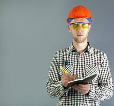 Tesisatçı veya genç bir işçi kask ve gözlük sipariş yazmak için hazır. 