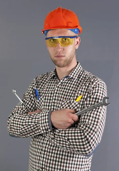 Moderno joven trabajador en casco sostiene dos llaves sobre fondo gris —  Fotos de Stock