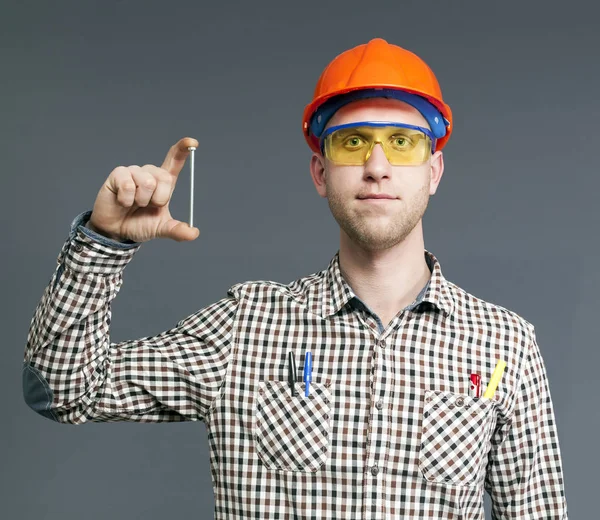 Um parafuso longo na mão de trabalhador jovem satisfeito em capacete e óculos . — Fotografia de Stock