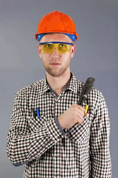 Υδραυλικός εργαλείο στα χέρια των εργαζόμενων νέων στο κράνος και γυαλιά. — Φωτογραφία Αρχείου