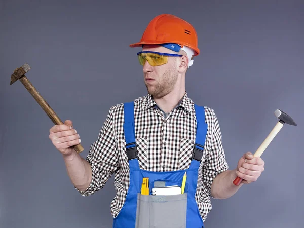 Joven trabajador sorprendido en uniforme con dos martillos en las manos . — Foto de Stock