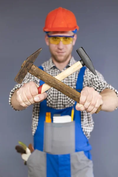 Jeune travailleur vigoureux en uniforme avec deux marteaux croisés dans les mains. Figure floue — Photo