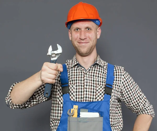 Usmíval se mladý dělník nebo instalatér v helmě drží klíč — Stock fotografie