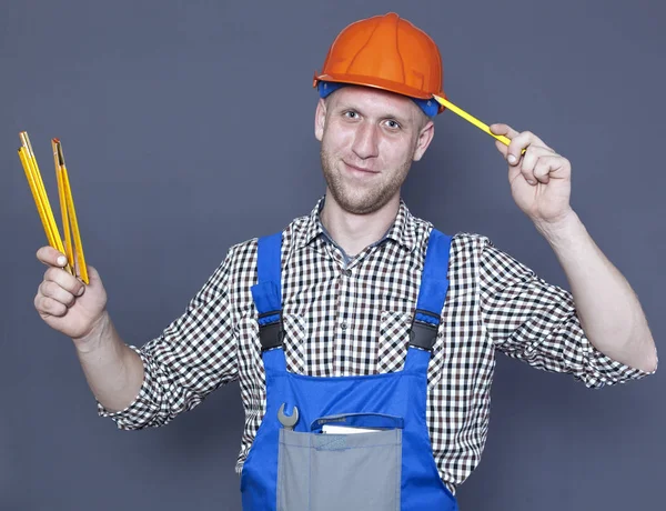 Улыбающийся молодой рабочий в шлеме держит карандаш и линейку на сером фоне — стоковое фото