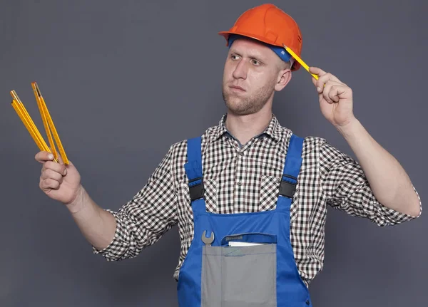 Молодой рабочий в шлеме держит карандаш и линейку на сером фоне — стоковое фото