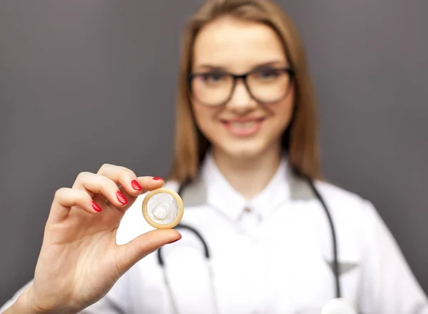 Joven doctora sonriente, enfermera en gafas con condón en la palma de la mano. Imagen conceptual — Foto de Stock