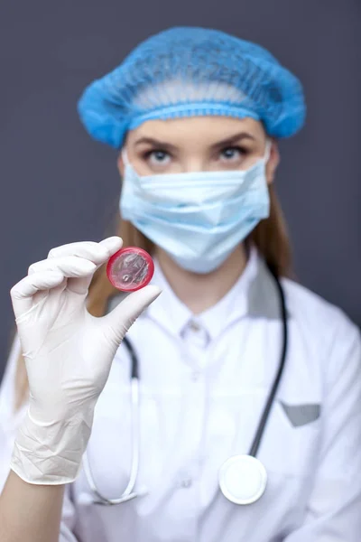 Mujer doctora, enfermera enmascarada con condón rojo en la palma. Imagen conceptual —  Fotos de Stock