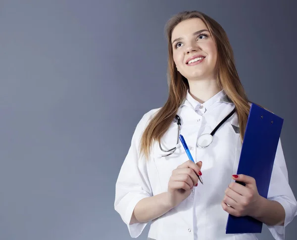 Atractivo médico mujer, enfermera sosteniendo tableta de papel y pluma, mirando hacia arriba — Foto de Stock