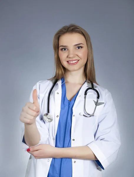 Jovem mulher atraente médico segura o dedo para cima e sorrir . — Fotografia de Stock