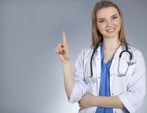 Joven mujer atractiva médico sostiene el dedo índice hacia arriba y sonrisa . — Foto de Stock