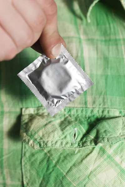 La mano del hombre con el condón en los dedos cerca de la camisa verde. De cerca. — Foto de Stock