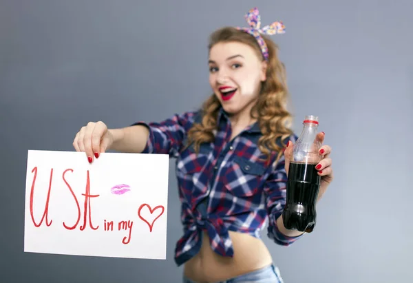 Jovencita sostiene cartel con lápiz labial beso y botella con bebida negra —  Fotos de Stock