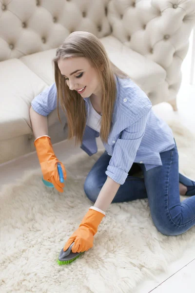 Attractive woman housewife cleans carpet with brush — Stock Photo, Image