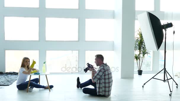 Fotoestudio detrás del escenario. Hombre fotógrafo explicar poses a mujer modelo como ama de casa . — Vídeo de stock