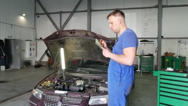 Soporte de la pluma del triunfo 4K.Mechanic cerca del coche en la sala de reparación del coche — Vídeo de stock