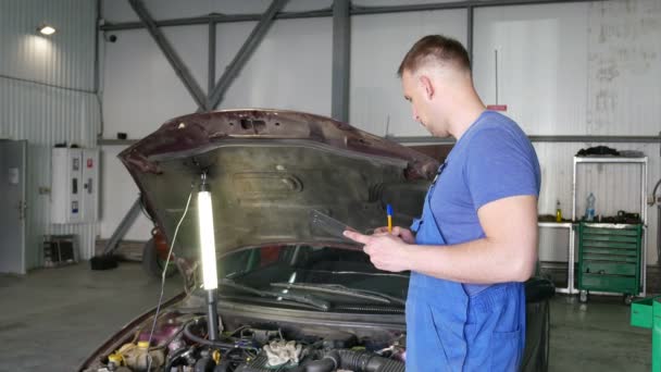 4k. Stand van de monteur in de buurt van auto in auto reparatie kamer en fotograaf. Backstage fotograferen proces — Stockvideo