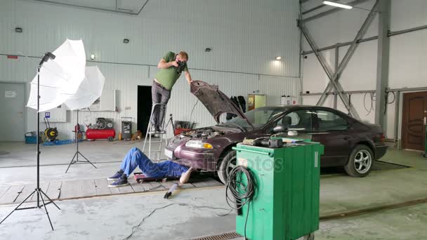 4К. Закулисный процесс фотографирования ремонтной бригады автомобиля. Механик под машиной — стоковое видео