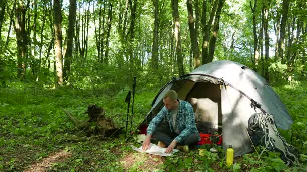 4k. Mann wandert mit Papierkarte neben Zelt im Frühlingswald. — Stockvideo