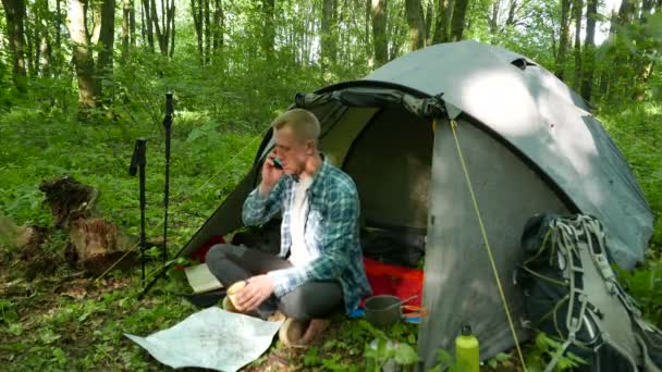 4K. Hombre excursionista charla turística por teléfono inteligente cerca de la tienda en el bosque de primavera. Equipo de turismo — Vídeo de stock