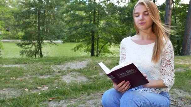 4k. Fiatal lány modern Biblia parkban. Keresztény csapat, a csúszik shot — Stock videók