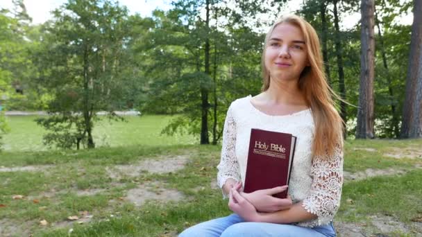 4k. Μοντέρνα κοπέλα με την Αγία Γραφή στο πάρκο. Χριστιανική ομάδα, ρυθμιστικό πυροβόλησε — Αρχείο Βίντεο