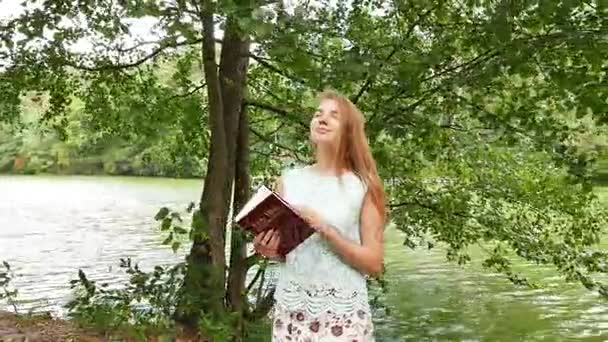 在公园里有魅力的年轻女孩手中的基督教圣经 — 图库视频影像