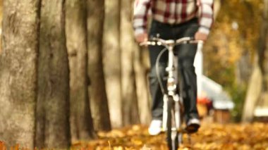 Ağır çekim. Adam binmek bisiklet sarı yaprakları ile sonbahar Park.