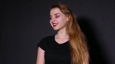 Genç güzel kız dalgalar saç koyu arka plan üzerinde gülümseyen. Ağır çekim