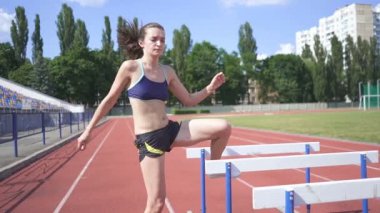 Ağır çekim. Bariyerlerin yanındaki stadyum antrenmanında genç bayan atlet. Sabit çekim.