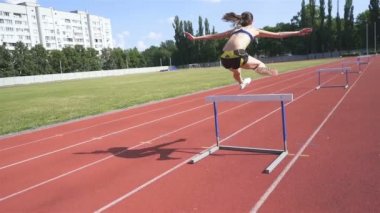 Pistteki bayan sporcu. Stadyumdaki genç koşucu engellerden atlıyor. Yavaş çekim, sabit çekim.