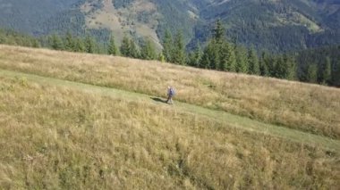 4K Havacılık. Sırt çantalı bir turist dağın eteklerinde uçuyor. Açık hava zamanı.