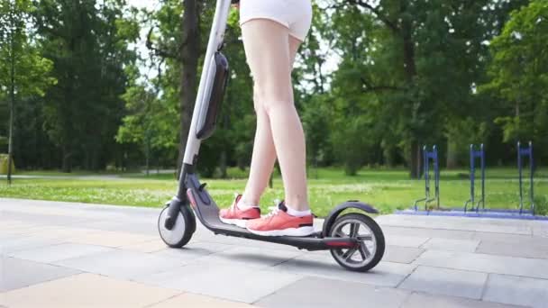 女の子の足 市内公園エリアで電動スクーターに乗る 着実に撃たれゆっくりと動き — ストック動画