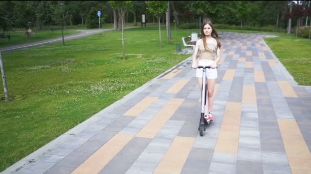 市内の公園エリアで電動スクーターに乗って若いかなり女の子 定常的に撃たれスローモーション — ストック動画
