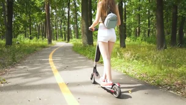 スローモーション 市内公園エリアで電動スクーターに乗って若いセクシーな女の子 バックビュー — ストック動画