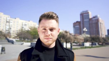 Tarz sahibi, genç, ciddi, beyaz bir adam sokakta dikilip kameraya bakıyor. Şehir portresi 