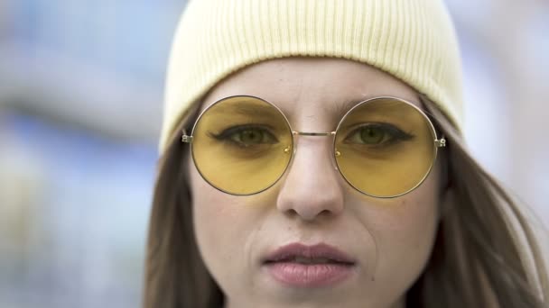 年轻而严肃的女孩戴着黄色的帽子和眼镜站在市区 近景肖像 — 图库视频影像