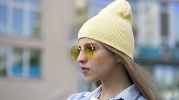 Ein Junges Mädchen Mit Gelber Mütze Und Brille Steht Stadtgebiet — Stockvideo