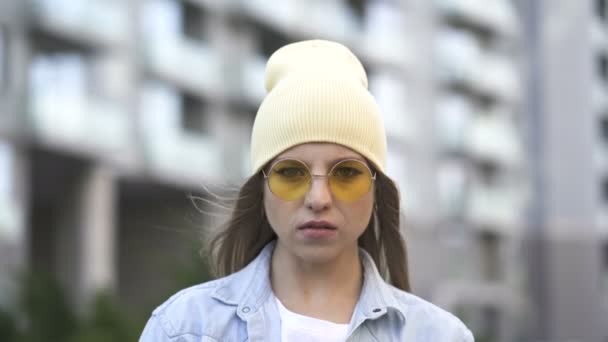 戴着黄色帽子和眼镜的小女孩站在市区 看着相机 街头肖像 — 图库视频影像