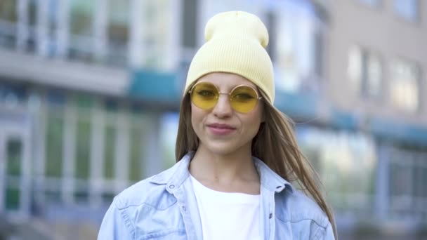 城市地区站着一个头戴黄帽 戴黄眼镜的年轻而积极的姑娘 街头肖像 — 图库视频影像