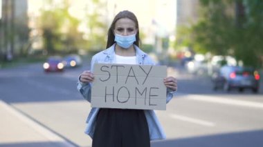 Ağır çekim. Maskeli genç bir kadın şehir sokaklarında posterle protesto ediyor. Kelime salgını ekibi
