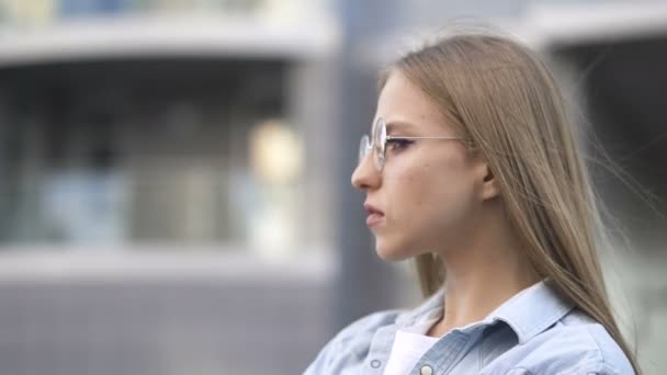 一个戴着圆形眼镜的严肃的小女孩站在市区 看着镜头 街头肖像 — 图库视频影像
