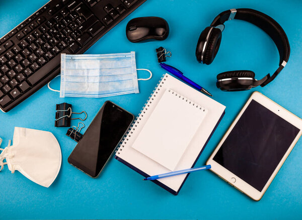 Дистанционное домашнее рабочее место и медицинская маска. Рабочее пространство для дистанционного обучения и работы в условиях карантина и самоизоляции. Рабочий стол с канцелярскими принадлежностями, телефон, компьютер. Работа из дома. Вид сверху
.