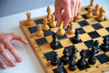 Evde masa oyunu. Bir çocuk tek başına satranç oynar. Eski tahta satranç tahtası. Çocuk elleri. Satranç tahtasındaki satranç taşları.