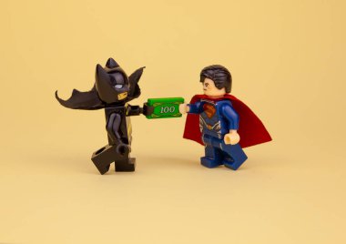 lego minifigures. Batman gives Superman a hundred dollars. Get paid in cash. To give a bribe. clipart