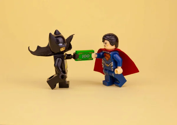 lego minifigures. Batman gives Superman a hundred dollars. Get paid in cash. To give a bribe.