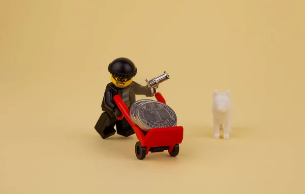 銃を持ったレゴの強盗が車輪の上のコインを奪う レゴ男のミニフィギュアはトロリーにお金を運んでいる — ストック写真