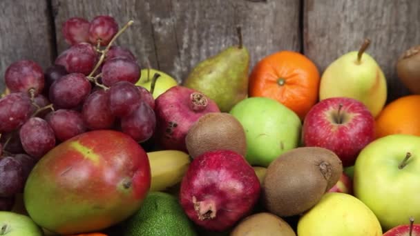 木製のキッチンテーブルの上に異なる果物のセット バナナ マンゴー リンゴ アボカド キウイ ザクロ みかん オレンジ ビタミン食品 — ストック動画