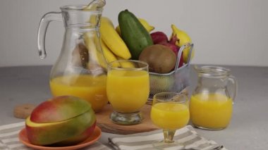 Bir bardak meyve suyu. Sarı ferahlatıcı yaz içkileri. Taze mango suyu, portakal suyu. Meyve sepeti masanın üstünde. Mutfakta taze meyve ve meyve suyu var. Vejetaryen yemeği. Vitamin içeceği. Muz, kivi, limon.